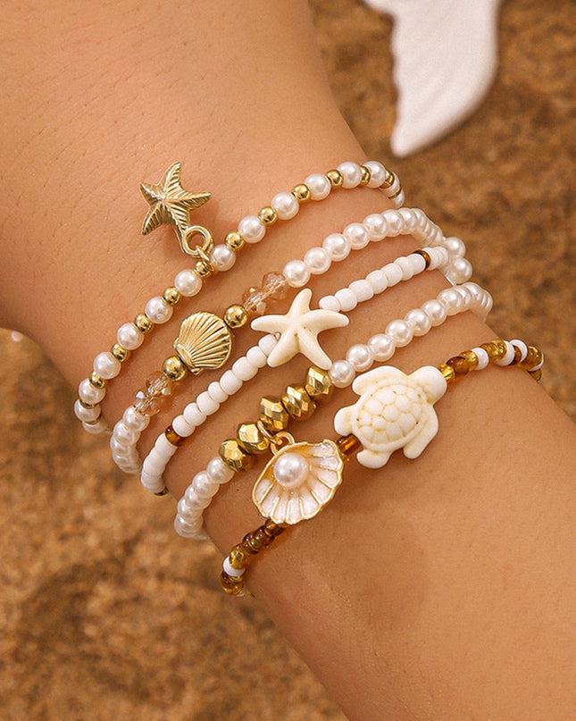 Close-up of a wrist wearing multiple pearl and shell bracelets on a sandy background
