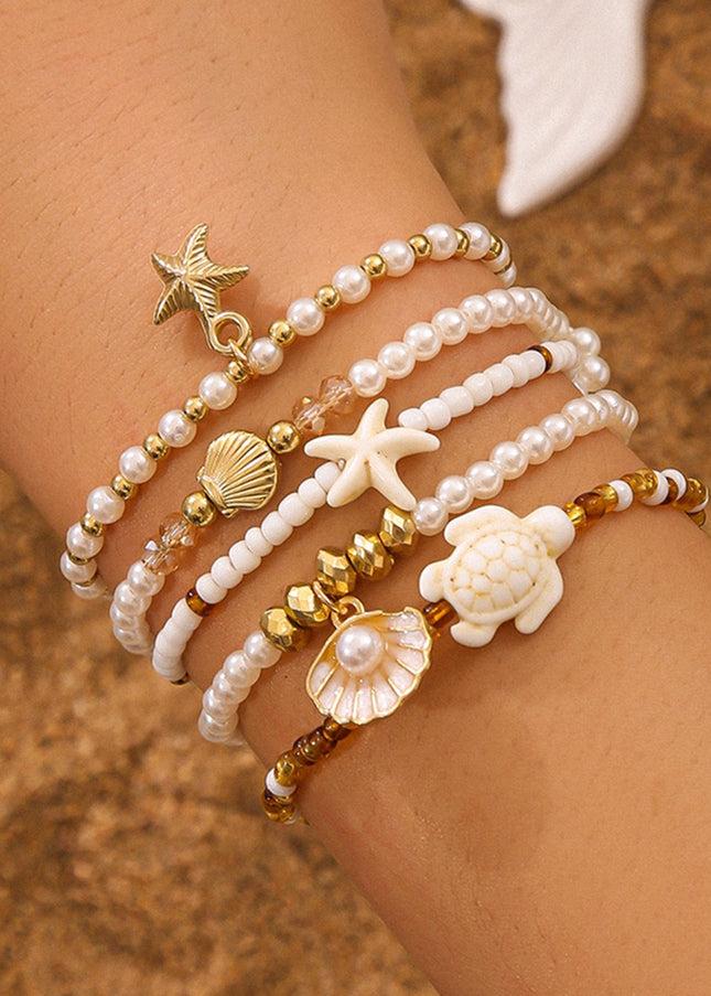 Close-up of a wrist wearing multiple pearl and shell bracelets on a sandy background