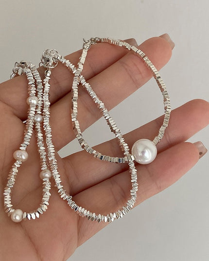 Hand holding a silver beaded bracelet with pearls against a neutral background