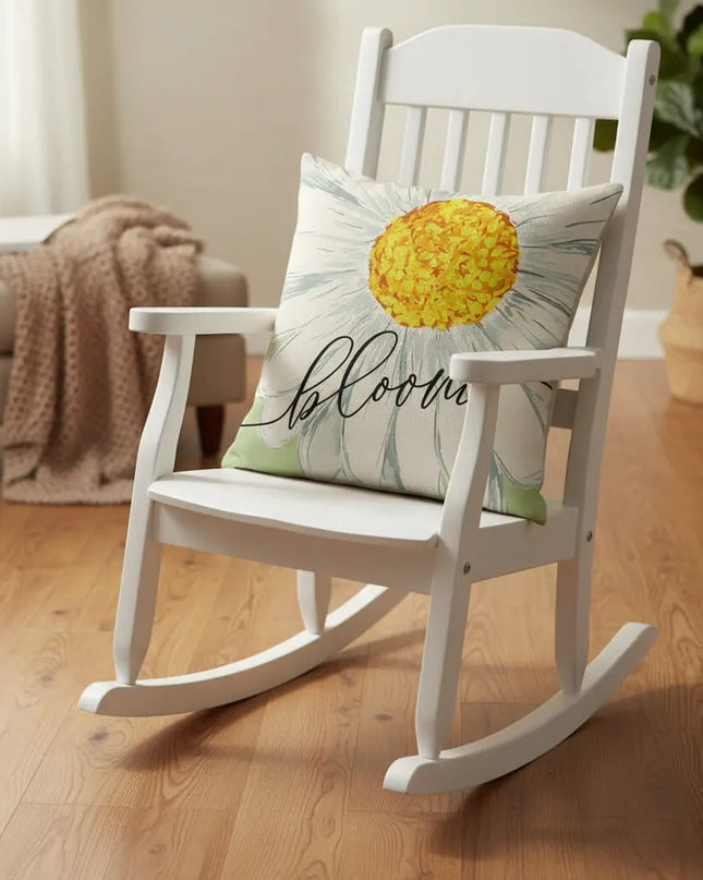 White rocking chair with a decorative pillow featuring a daisy design and the word 'bloom' in a cozy room.