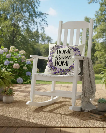 White rocking chair with a 'Home Sweet Home' pillow on a porch with plants and flowers.