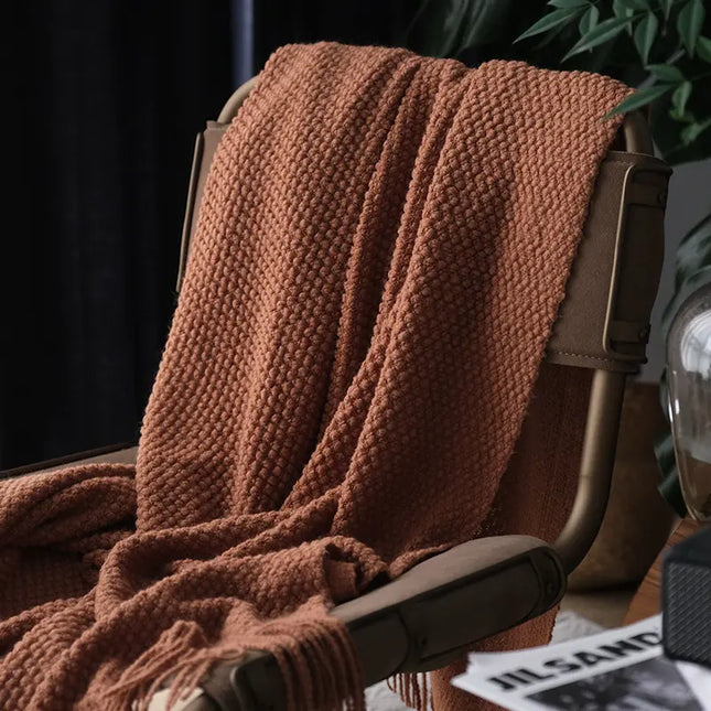 Brown knitted blanket draped over a chair with a blurred background