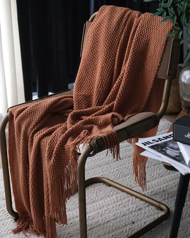 Brown knitted blanket draped over a chair with a blurred indoor background