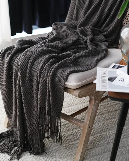 Dark gray textured throw blanket draped over a chair with a side table in the background.