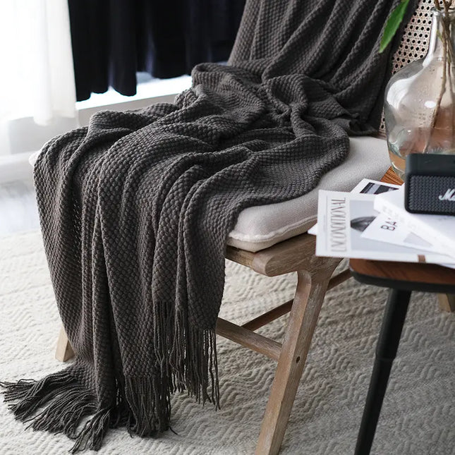 Dark gray textured throw blanket draped over a chair with a side table in the background.