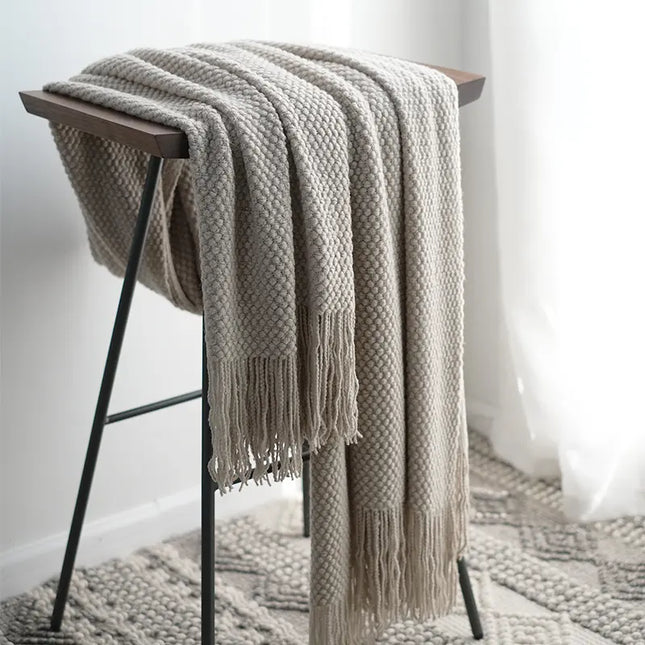 Light gray knitted blanket draped over a wooden stool in a minimalistic room.