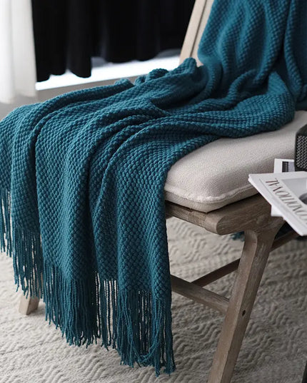 Teal blanket with fringe draped over a chair in a room setting.
