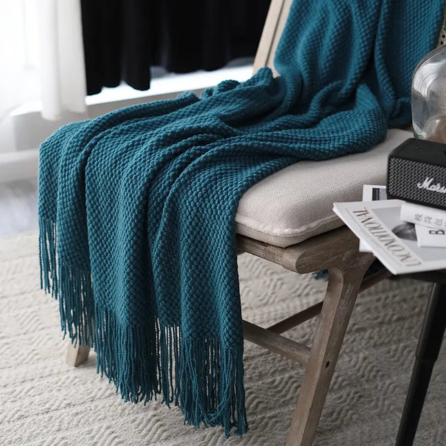 Teal blanket with fringe draped over a chair in a room setting.