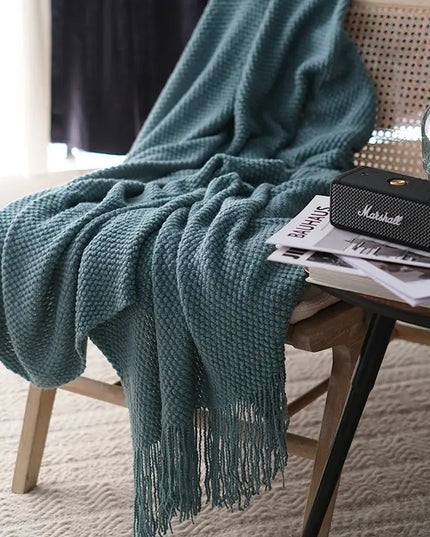 Grey-blue blanket draped over a chair with a Marshall speaker and magazines on a table.