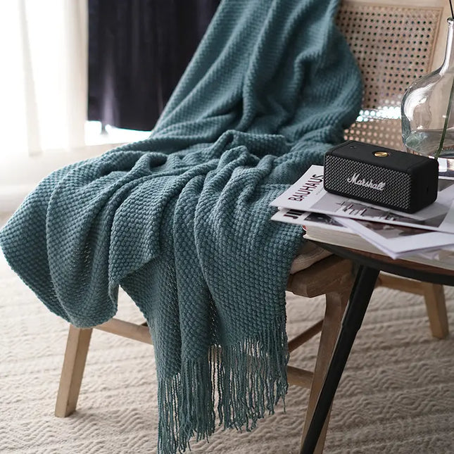 Grey-blue blanket draped over a chair with a Marshall speaker and magazines on a table.