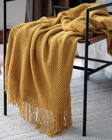 Yellow knitted blanket draped over a chair on a light-colored floor.