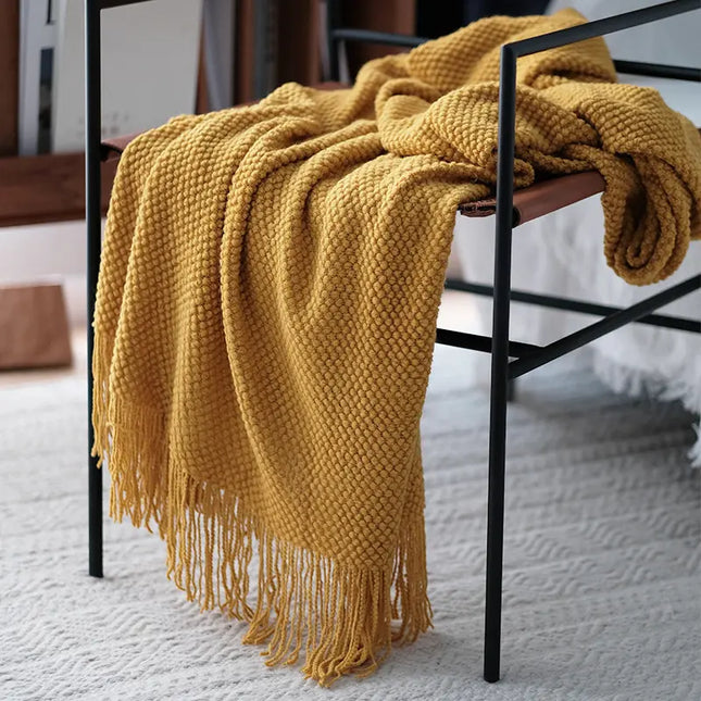 Yellow knitted blanket draped over a chair on a light-colored floor.