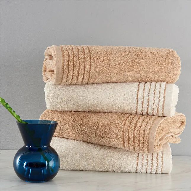 Stack of beige and white towels with a blue vase on a gray background