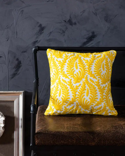 Yellow patterned pillow on a dark brown leather chair against a dark gray wall.