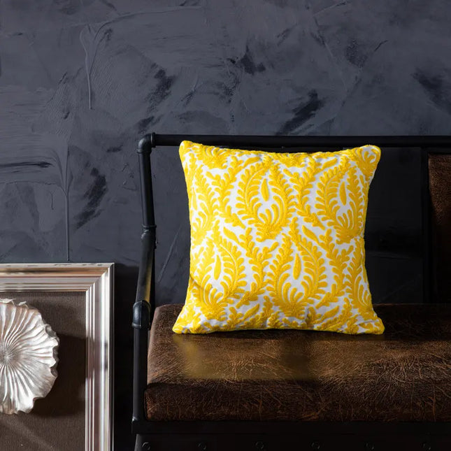 Yellow patterned pillow on a dark brown leather chair against a dark gray wall.