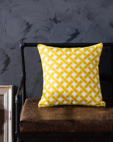 Yellow and white patterned pillow on a brown cushion against a dark wall.