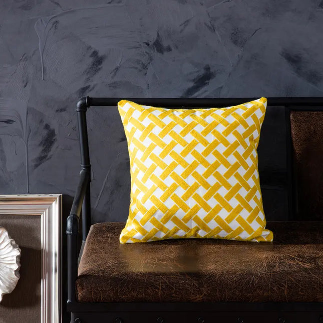 Yellow and white patterned pillow on a brown cushion against a dark wall.