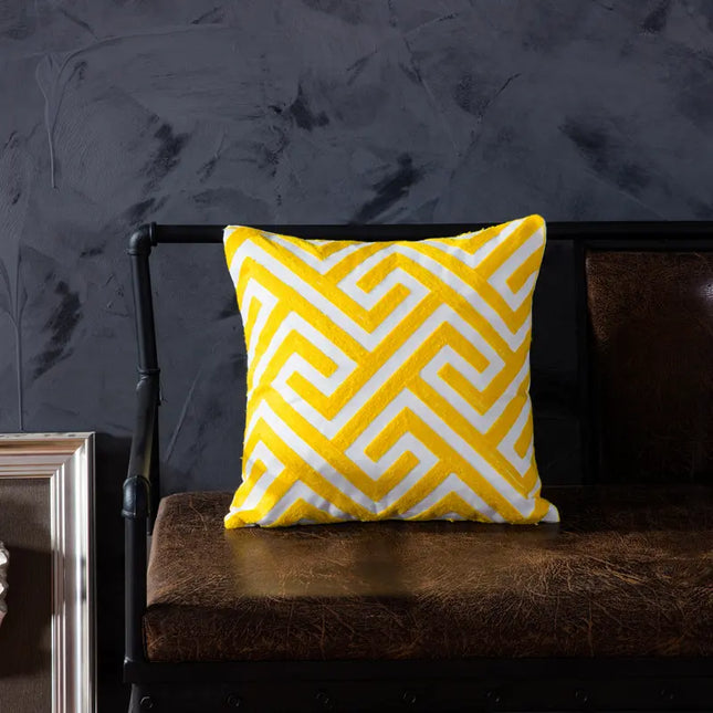 Yellow and white patterned pillow on a dark bench against a dark wall.