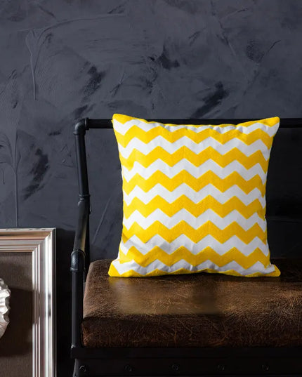 Yellow and white chevron patterned pillow on a dark brown chair against a dark gray wall.