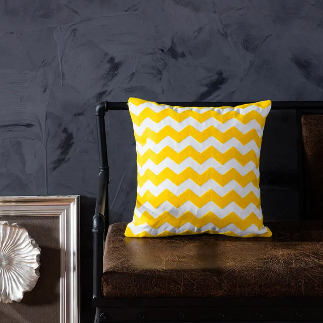 Yellow and white chevron patterned pillow on a dark brown chair against a dark gray wall.