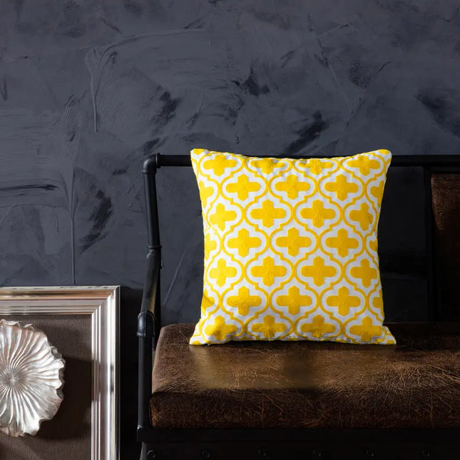 Yellow patterned pillow on a dark brown chair against a textured dark gray wall.
