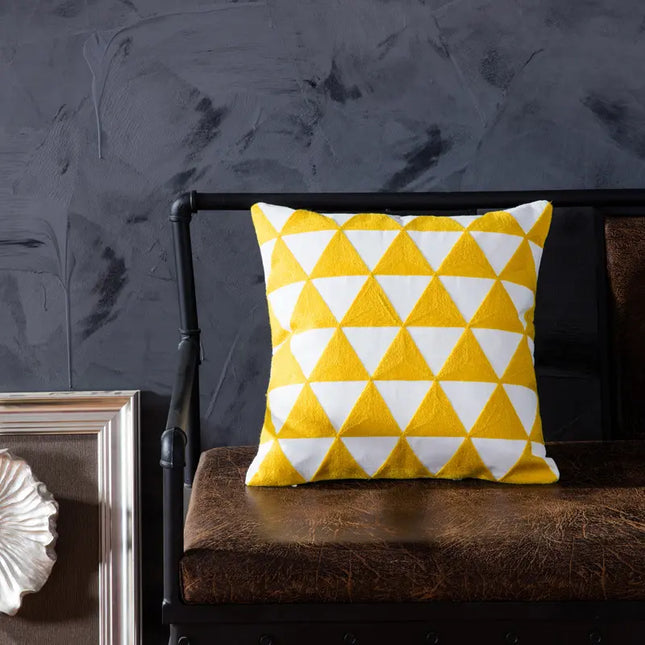Yellow and white geometric pillow on a brown cushion against a dark textured wall.