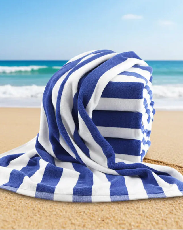 Blue and white striped towel on a sandy beach with ocean in the background