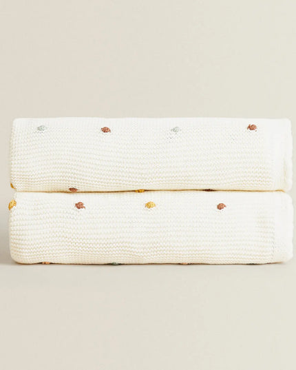 White knitted blanket with gold accents on a beige background
