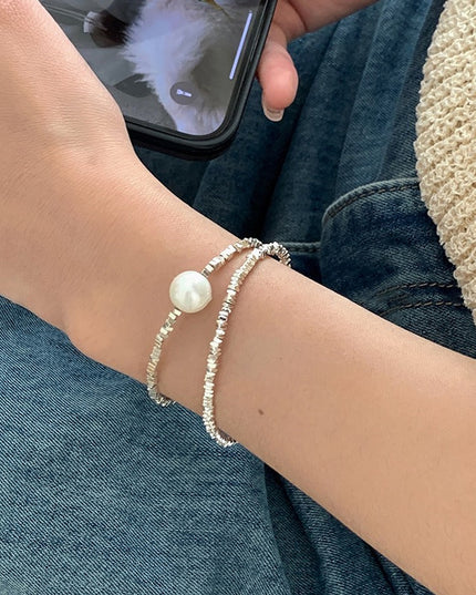 Close-up of a wrist wearing two pearl bracelets with a denim background.