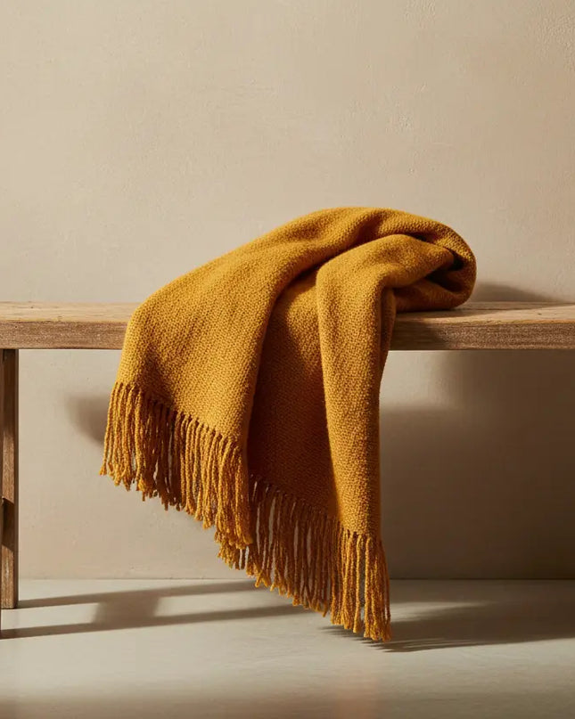 Wooden bench with a mustard yellow blanket draped over it against a beige wall.