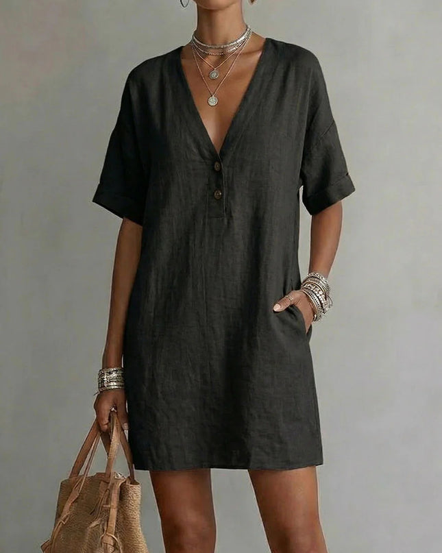 Woman wearing a khaki dress holding a brown bag against a plain background