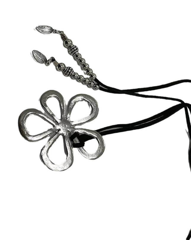 Metal flower-shaped pendant on a black cord against a white background