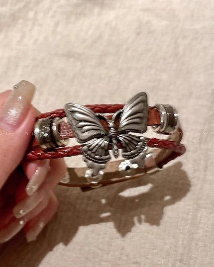 Butterfly-themed bracelet with red cord held by a hand on a beige background