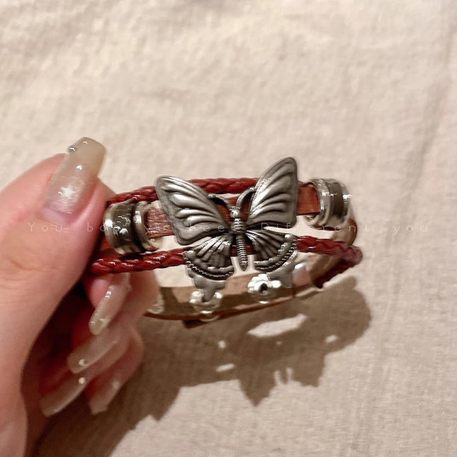 Butterfly-themed bracelet with red cord held by a hand on a beige background