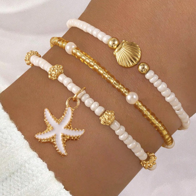 Three beaded bracelets with gold and white beads and starfish charm on a wrist.