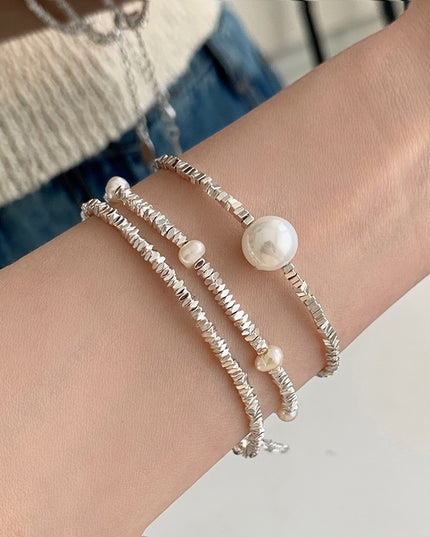 Close-up of a wrist wearing two pearl bracelets on a neutral background