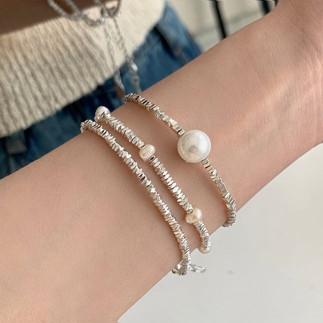Close-up of a wrist wearing two pearl bracelets on a neutral background