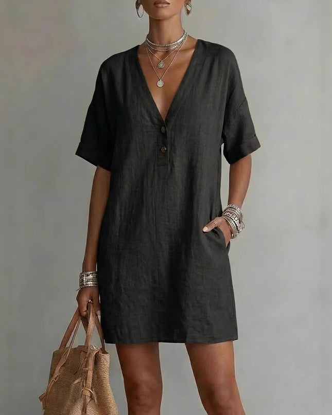 Woman wearing a black dress holding a woven bag against a plain background