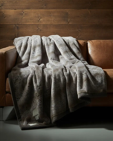 Dark gray blanket draped over a brown leather sofa against a wooden wall.