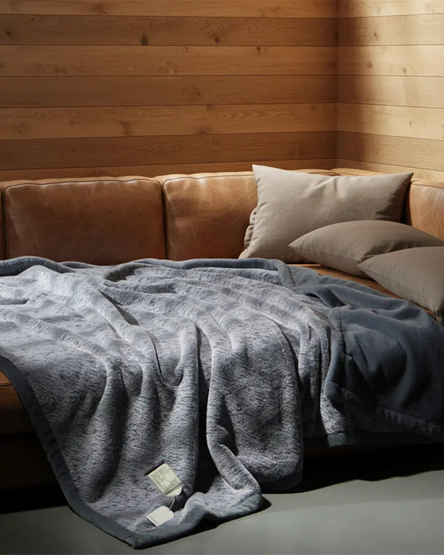 Gray blanket draped over a brown sofa with wooden walls in the background