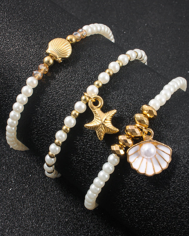 Three pearl bracelets with gold charms on a black background