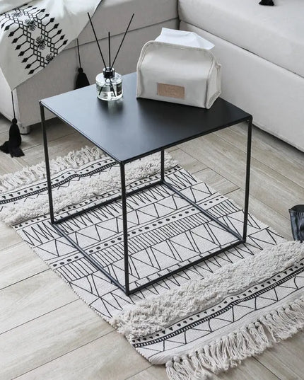 Black metal side table with decorative items on a patterned rug in a living room.