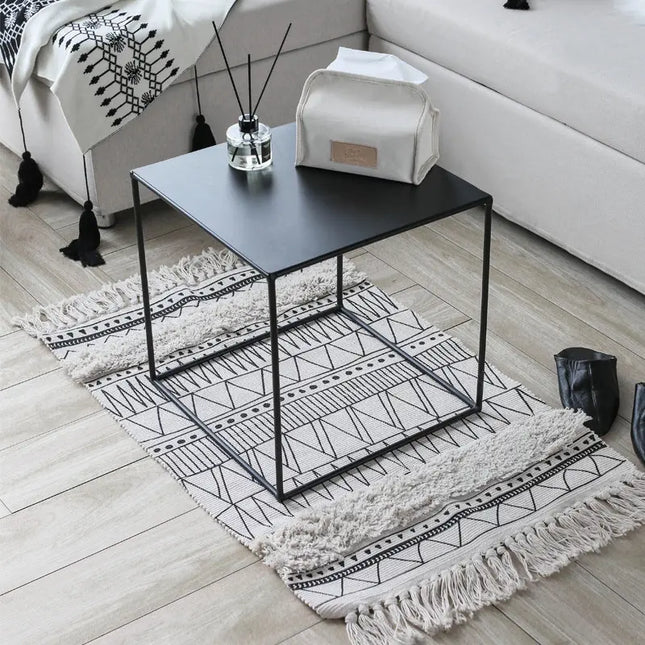 Black metal side table with decorative items on a patterned rug in a living room.