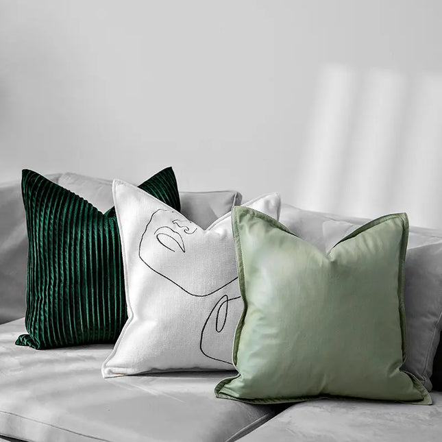 Three decorative pillows on a sofa with a neutral background