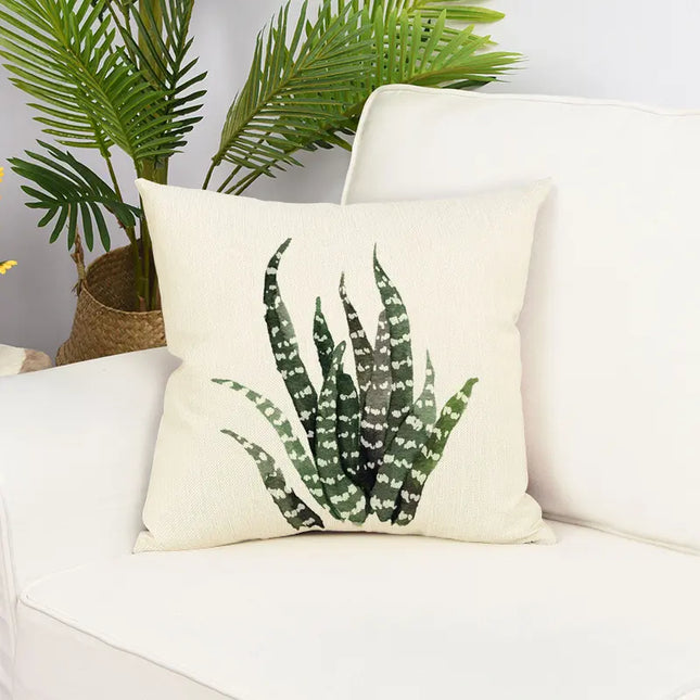Decorative pillow with aloe vera plant design on a white couch with plants in the background