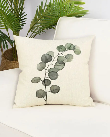 Decorative pillow with eucalyptus design on a white couch with plants in the background