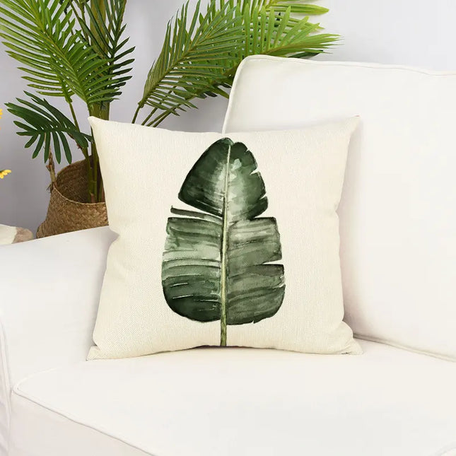 Decorative pillow with a green leaf design on a white couch with plants in the background.