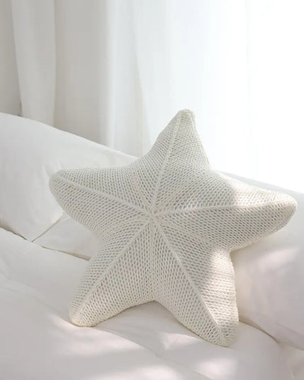 Star-shaped knitted pillow on a white bed with curtains in the background