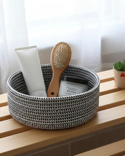 Woven black and white basket with hairbrush and bottle on a wooden surface with white curtains in the background