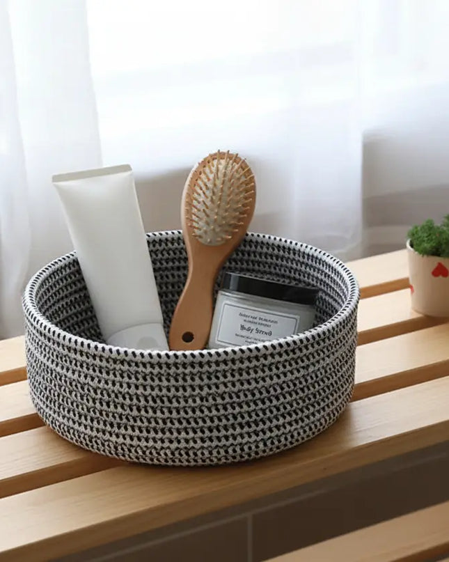 Woven black and white basket with hairbrush and bottle on a wooden surface with white curtains in the background
